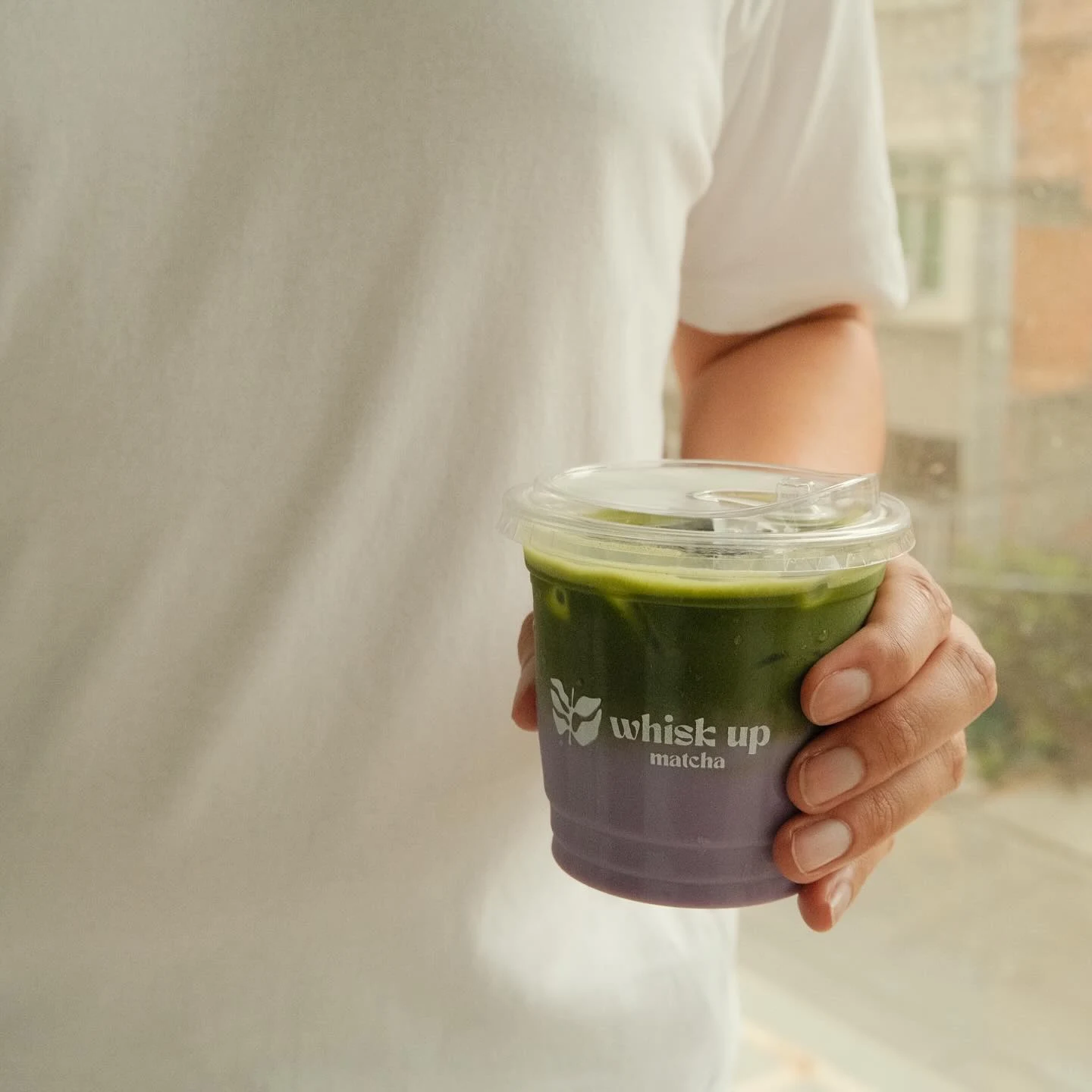 Whisk Up Matcha branded cup held in hand